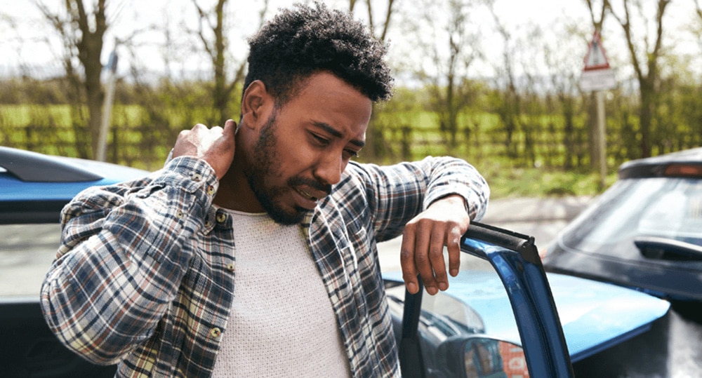Man holding his neck as he leans on his car door after a collision
