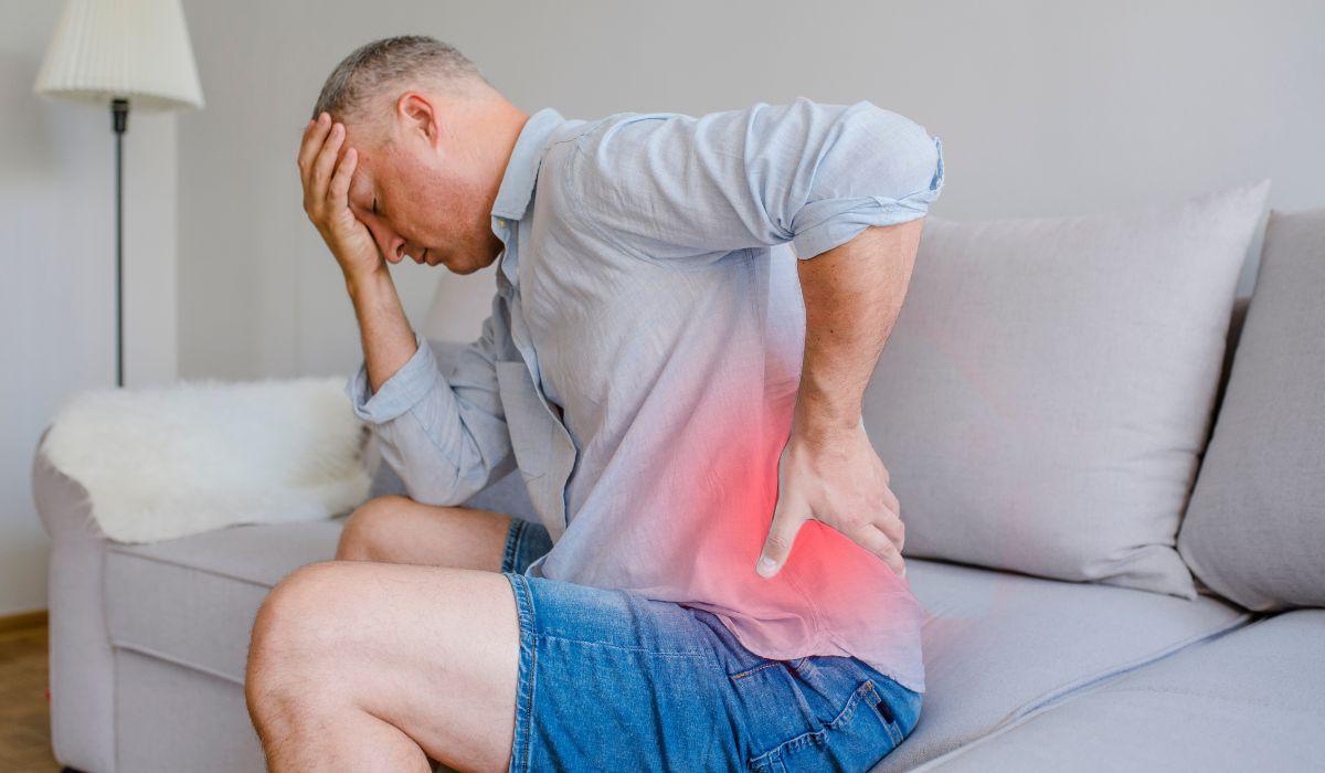 Man on a sofa holding his head and his sore lower back